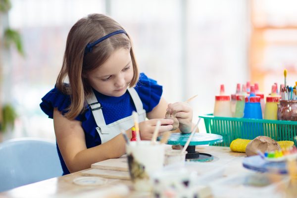 Child working on pottery wheel. Kids arts and crafts class in workshop. Little girl creating cup and bowl of clay. Creative activity for young children in school. Cute child forming toy with ceramic.